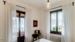A bedroom with a bed, a radiator, a window with curtains, a picture frame on the wall, and a view of the outside. - Menaggio at its best - MyHomeinComo (Menaggio)