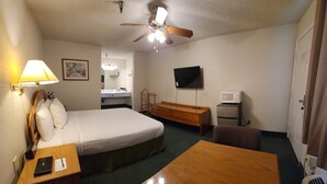 A hotel room with a bed, a desk, a chair, a TV, a microwave, and a ceiling fan. - Formosa Inn (Fresno)