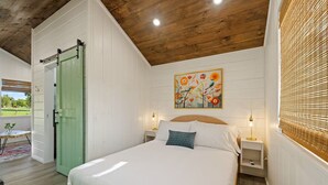 Een slaapkamer met een houten plafond, een groene deur, een bed met witte beddengoed, een aan de muur hangend schilderij en nachtlampjes.
