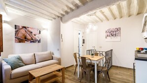 Ein Wohnzimmer mit einer Couch, einem Holztisch, einem Esstisch mit Stühlen und einer Küchenzeile mit Arbeitsplatte und Schränken.