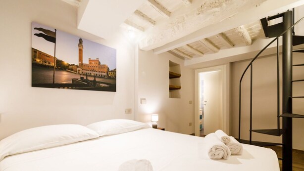 Ein Hotelzimmer mit einem Bett, einem Stadtbildgemälde, einer Treppe und einer Tür zu einem anderen Raum.