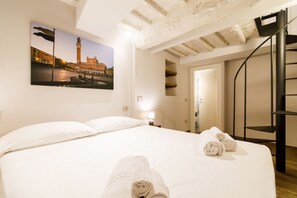 A hotel room with a bed, a painting of a cityscape, a staircase, and a door leading to another room.
