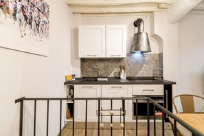 A kitchen with white cabinets, a stainless steel range hood, a sink, and a tiled backsplash.