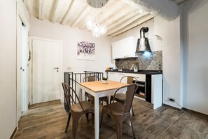 A dining area with a wooden table and chairs, a kitchen with white cabinets and a black countertop, and a ceiling with exposed beams.