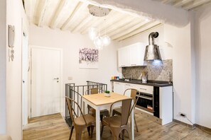 A compact kitchen with white cabinets, a wooden dining table, and a hanging light fixture.