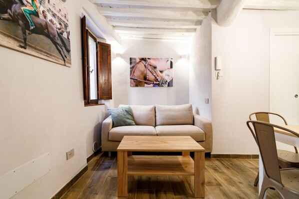 A room with a sofa, a wooden coffee table, a dining table with chairs, and two wall-mounted paintings.