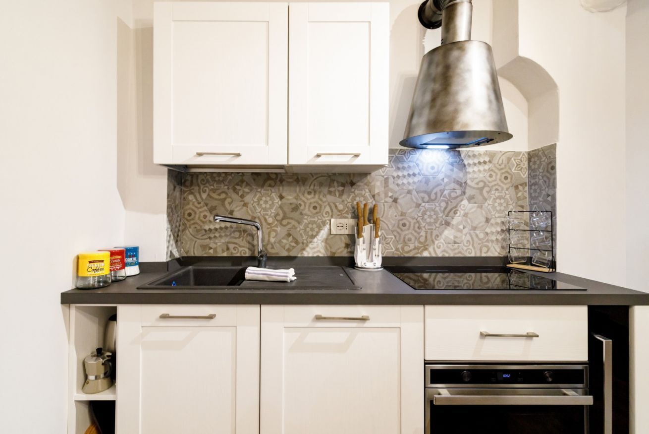 A kitchen with white cabinets, a black countertop, a stainless steel sink, and a built-in oven.