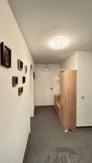 A hallway with a door at the end, a clock on the wall, and a wooden cabinet. - Daheim am Wasserturm – peace, style and a place to arrive and feel at home (Wörth am Rhein)