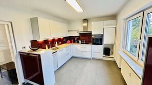 A modern kitchen with white cabinets, a built-in oven, and a window providing a view of the outdoors. - Daheim am Wasserturm – peace, style and a place to arrive and feel at home (Wörth am Rhein)