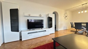 A modern living room with a flat-screen TV, white cabinetry, a dining area with a table and chairs, and a red rug. - Daheim am Wasserturm – peace, style and a place to arrive and feel at home (Wörth am Rhein)
