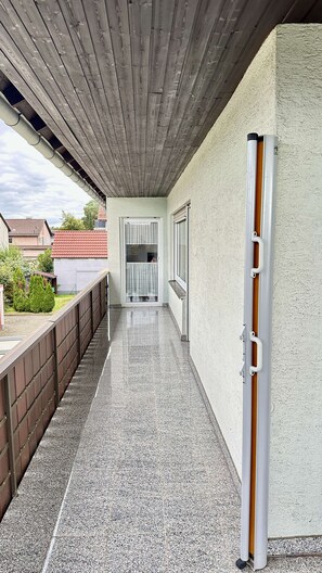 A covered outdoor corridor with a tiled floor, a wooden ceiling, and a view of a residential area in the background. - Daheim am Wasserturm – peace, style and a place to arrive and feel at home (Wörth am Rhein)
