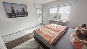 A bedroom with a bed, a radiator, a window with curtains, a door, and a picture on the wall. - Daheim am Wasserturm – peace, style and a place to arrive and feel at home (Wörth am Rhein)