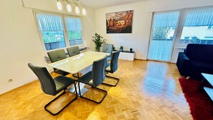 Een moderne woonkamer met een houten visgraatvloer, een grote eettafel met zes stoelen, een zwarte bank en een rood vloerkleed.