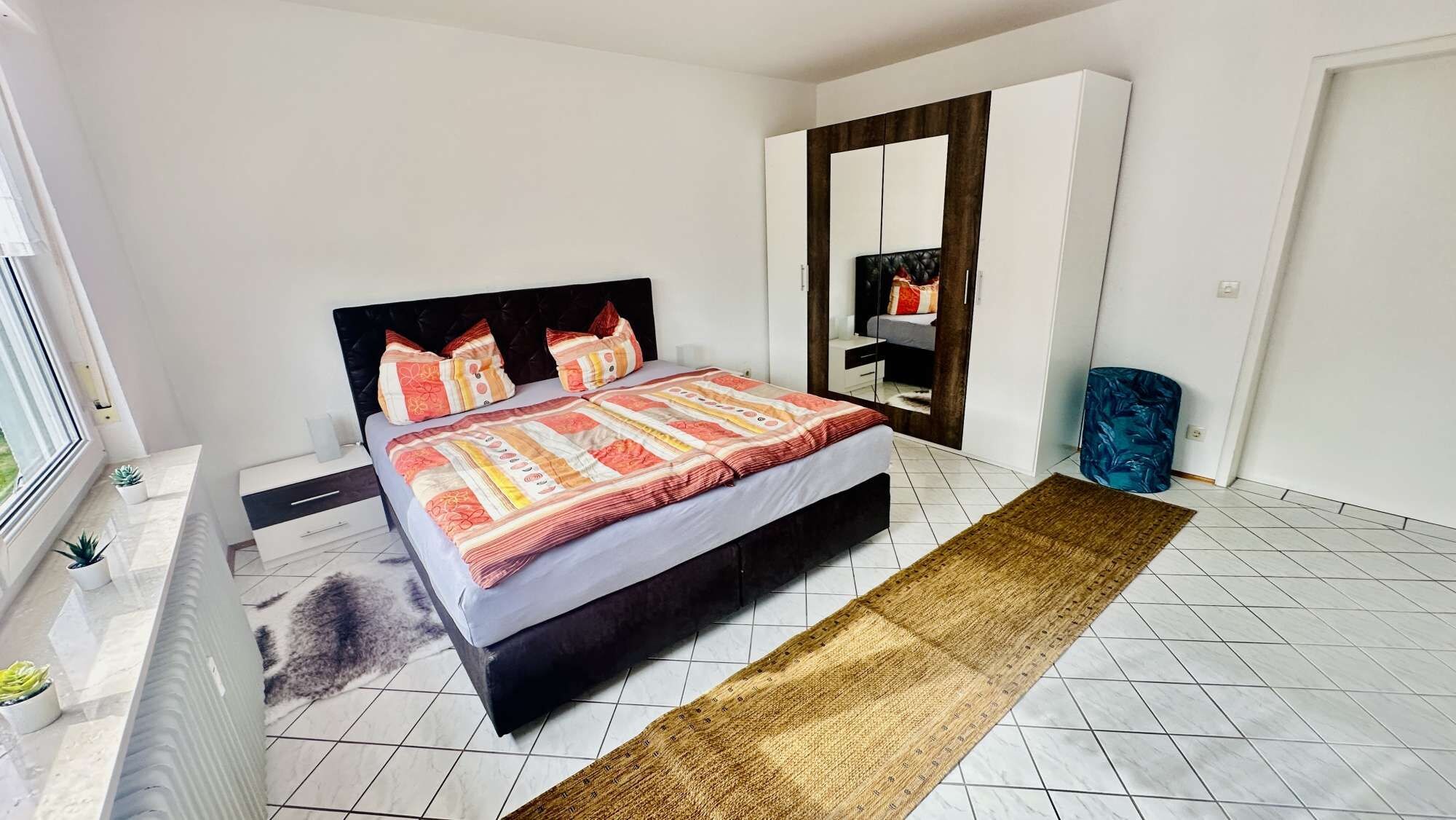 Ein modernes Schlafzimmer mit Bett, Nachttisch, Kommode, Spiegel und Fenster.