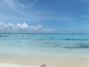 A beach with clear turquoise water, several boats, and a sandy shore.