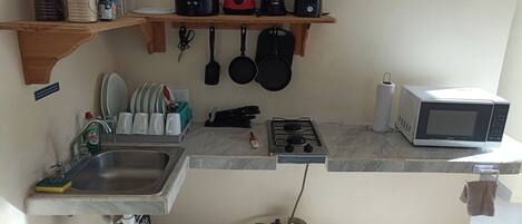 A compact kitchen with a sink, stove, microwave, and various utensils.