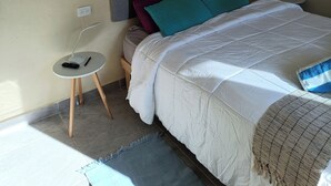 A bedroom with a bed, bedside table, lamp, air conditioner, and a wall-mounted power outlet. - Cómodo, céntrico a cuadra y media de playa norte (Isla Mujeres)