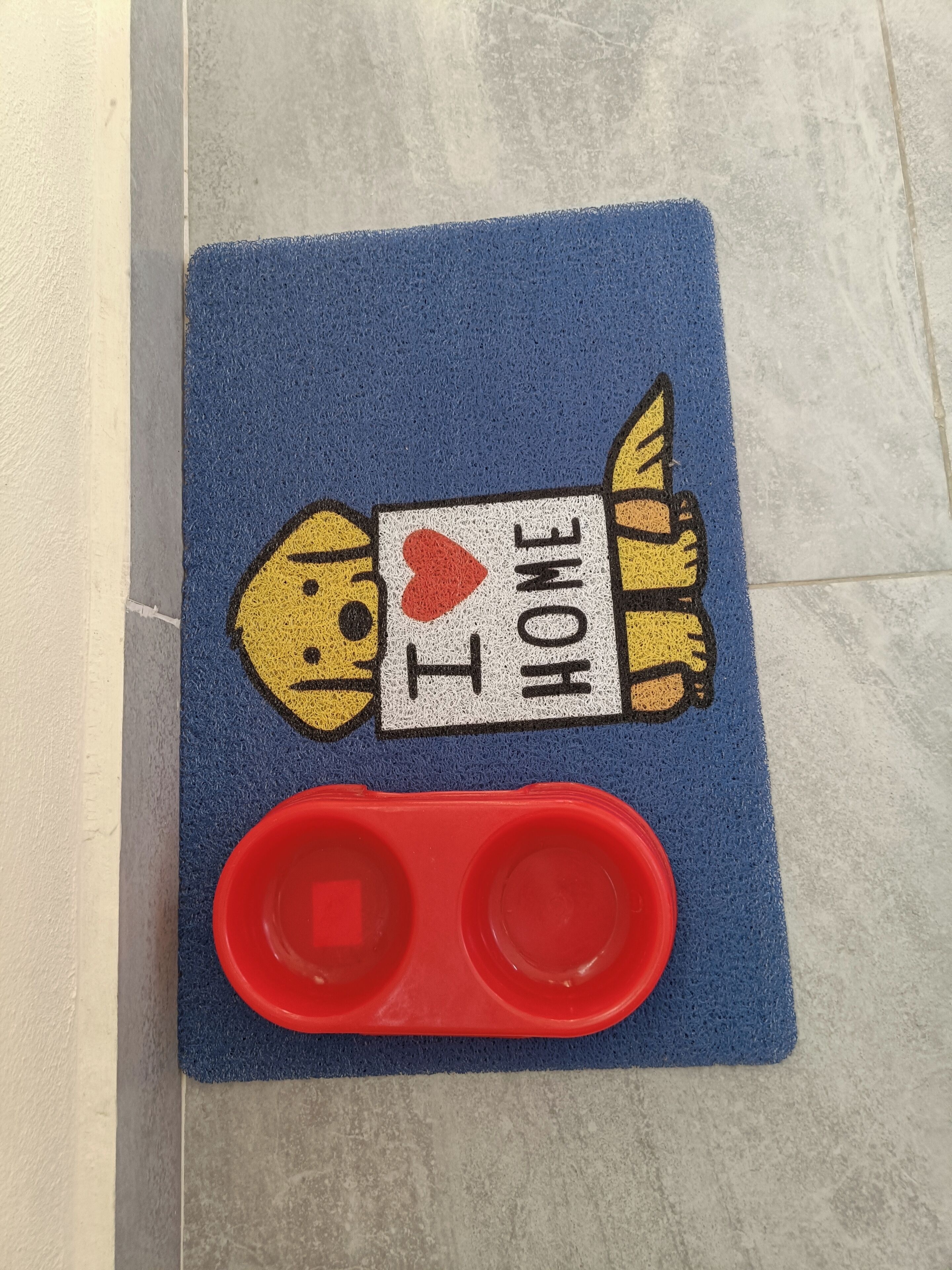 A blue mat with a cartoon dog and the text "I ♥ HOME" on it, placed on a tiled floor.