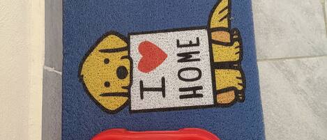 A blue mat with a cartoon dog and the text "I ♥ HOME" on it, placed on a tiled floor.