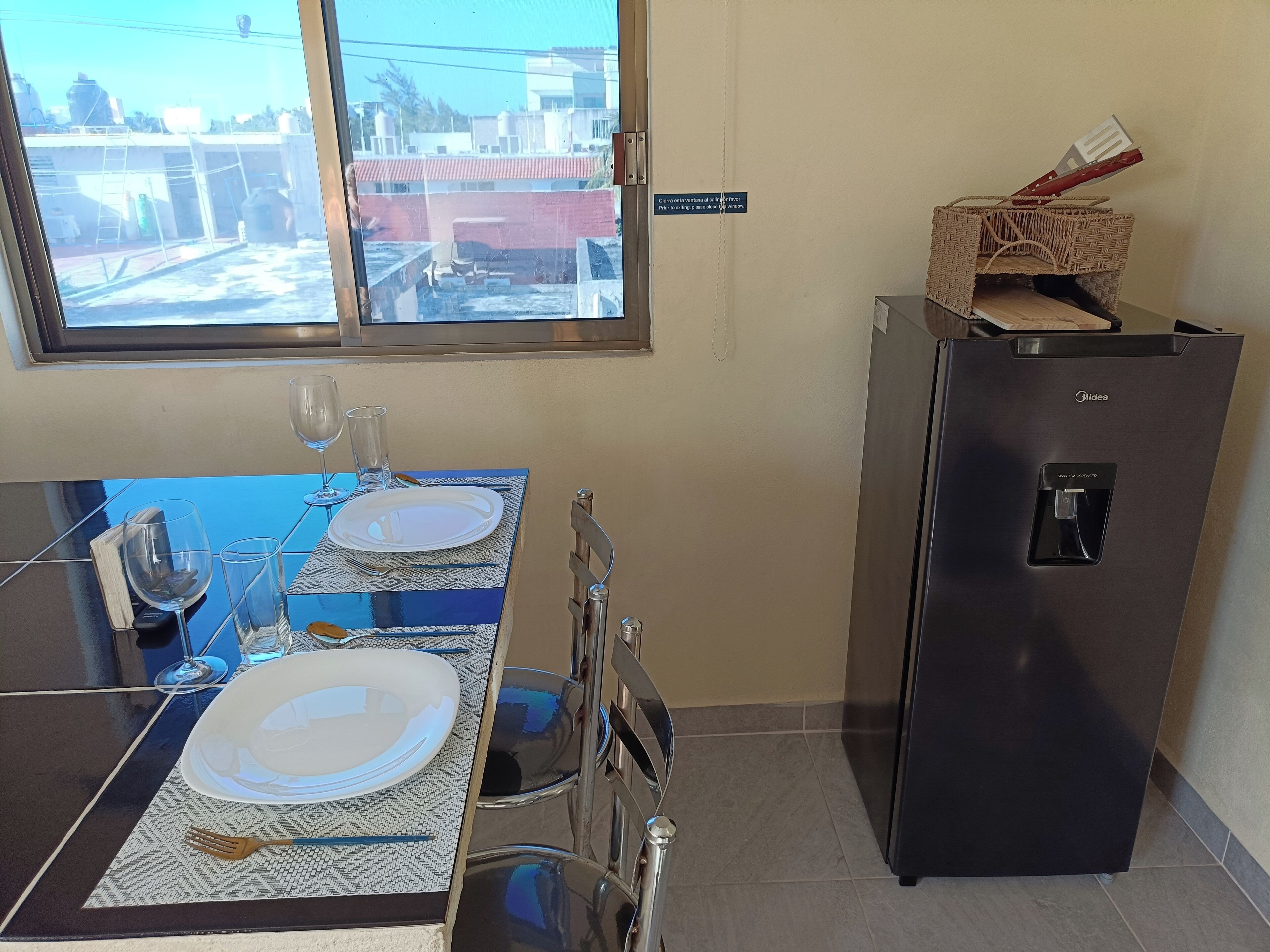 A dining area with a table set for two, a water dispenser, and a refrigerator.