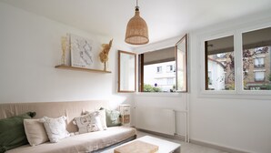 A modern living room with a beige sofa, a white coffee table, and a large window offering a view of buildings outside. - Appartement Lavoisier - Welkeys (Puteaux)