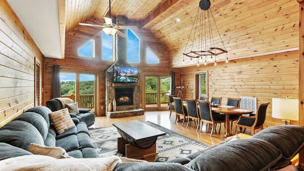 Un acogedor interior de cabaña con chimenea, zona de comedor y un ventanal grande con vistas al exterior.