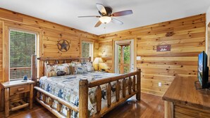 Un dormitorio de cabaña de madera con cama, mesita de noche y ventilador de techo.