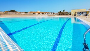 A clear blue swimming pool with lane dividers, surrounded by a fence and buildings in the background. - Amazing apartment in Le Barcarès (Le Barcarès)