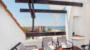 A balcony with a view of the sea, two striped chairs, a wooden table with a bottle and glasses, and a white wall with a shelf. - Amazing apartment in Le Barcarès (Le Barcarès)