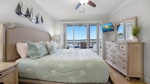 A bedroom with a large bed, a dresser, a ceiling fan, and a TV.