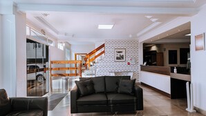 Uma sala de estar ampla com um sofá de couro preto, escada de madeira e uma área de cozinha com bancada de madeira.