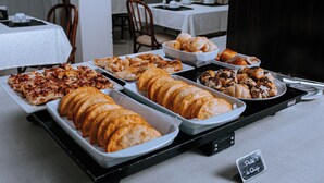 Mesa de buffet com diversos alimentos, incluindo pizzas, doces e pão.