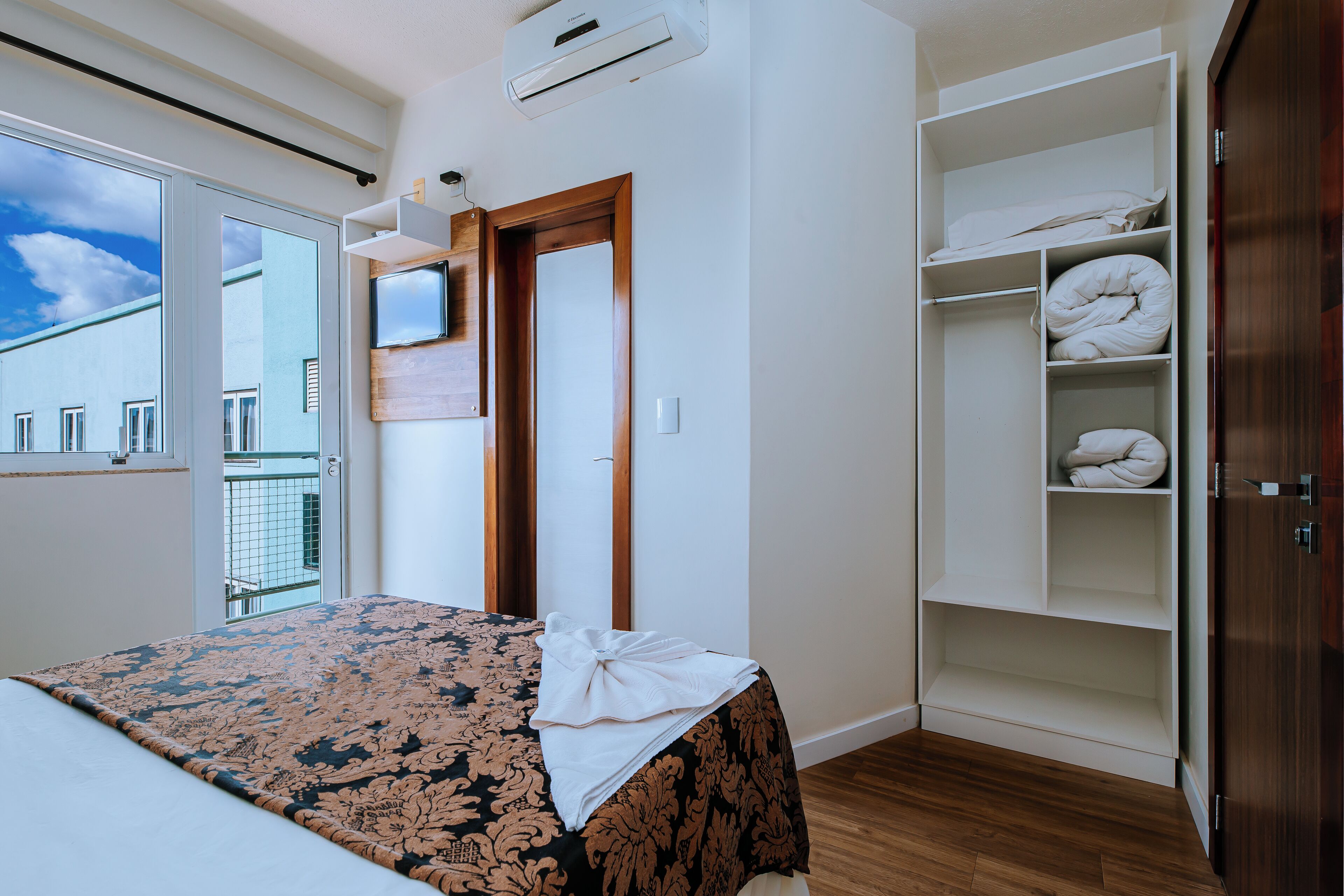A bedroom with a bed, a wardrobe, and a balcony.
