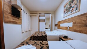 Quarto de hotel com duas camas, televisão, um quadro e cabeceira de madeira.