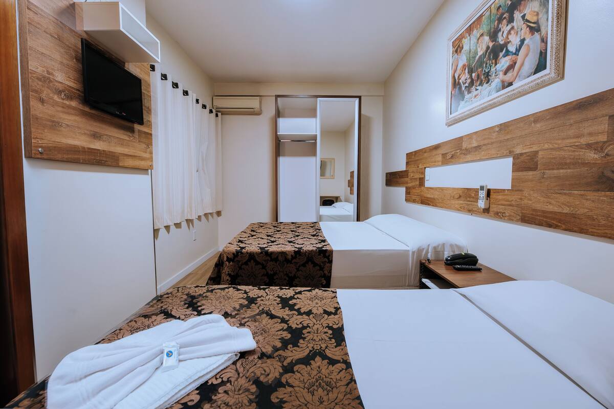 A hotel room with two beds, a TV, a painting, and a wooden headboard.