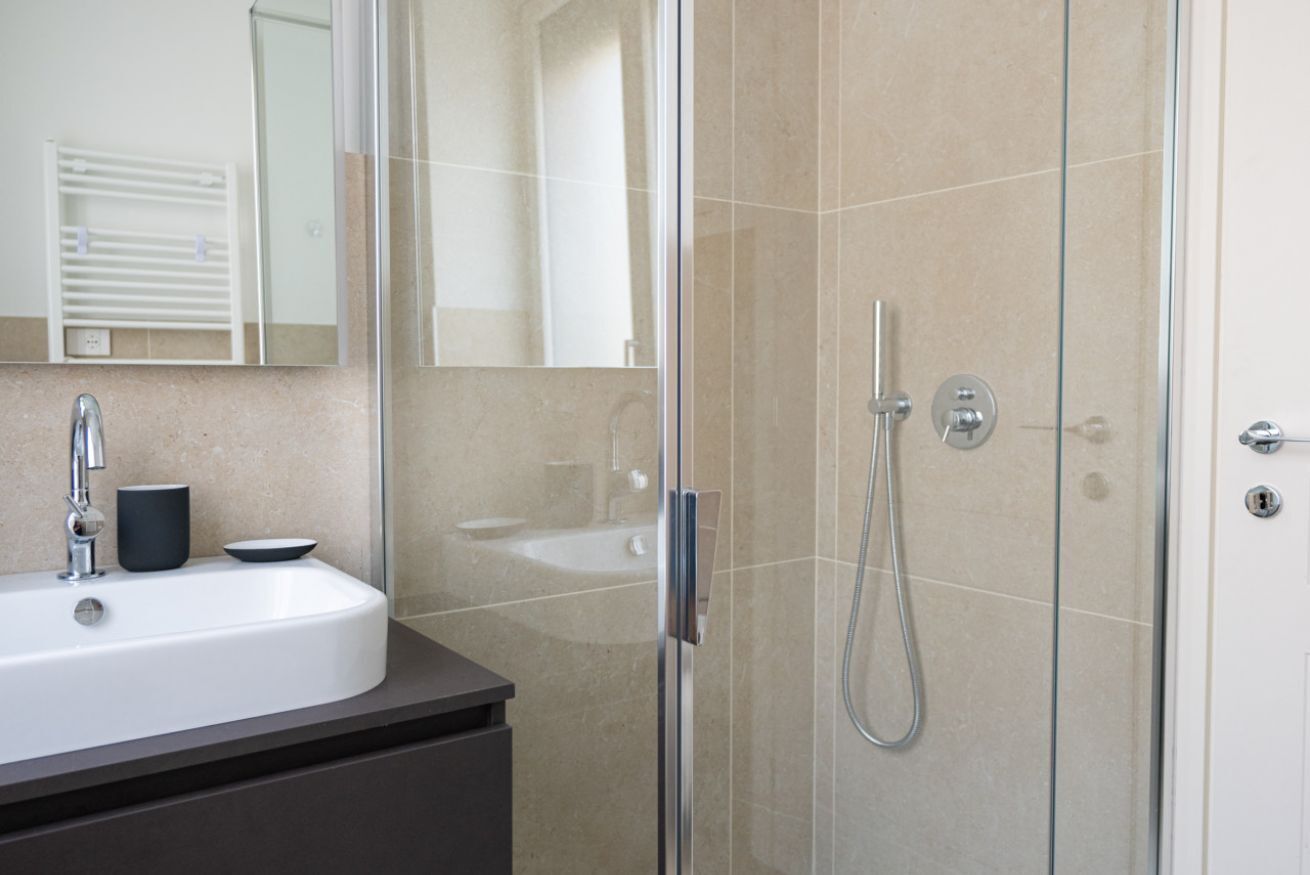 A modern bathroom with a glass-enclosed shower, a white sink, and a mirror above the sink.