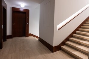 A hallway with a wooden door, a staircase with a wooden handrail, and a light fixture on the ceiling.