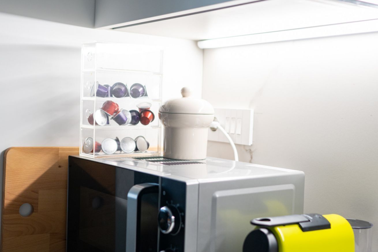 A kitchen with a coffee maker, a shelf with mugs, and a wooden cutting board.