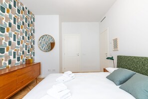 A hotel room with a bed, a wooden dresser, a round mirror, a door, and a green headboard.