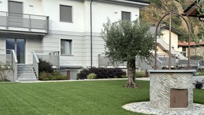 Un edificio moderno de dos pisos con un césped cuidado, un banco de piedra y una valla metálica.