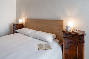 A neatly made bed with a wooden headboard, a bedside table with a lamp, and a cup on the nightstand.
