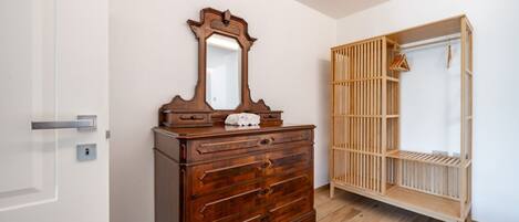 A room with a wooden dresser, a mirror, and a wooden wardrobe with shelves.