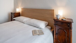 A neatly made bed with a wooden headboard, a bedside table with a lamp, and a cup on the nightstand. - Villa Sunset - with pool and large garden - few steps from the beach (Dervio)