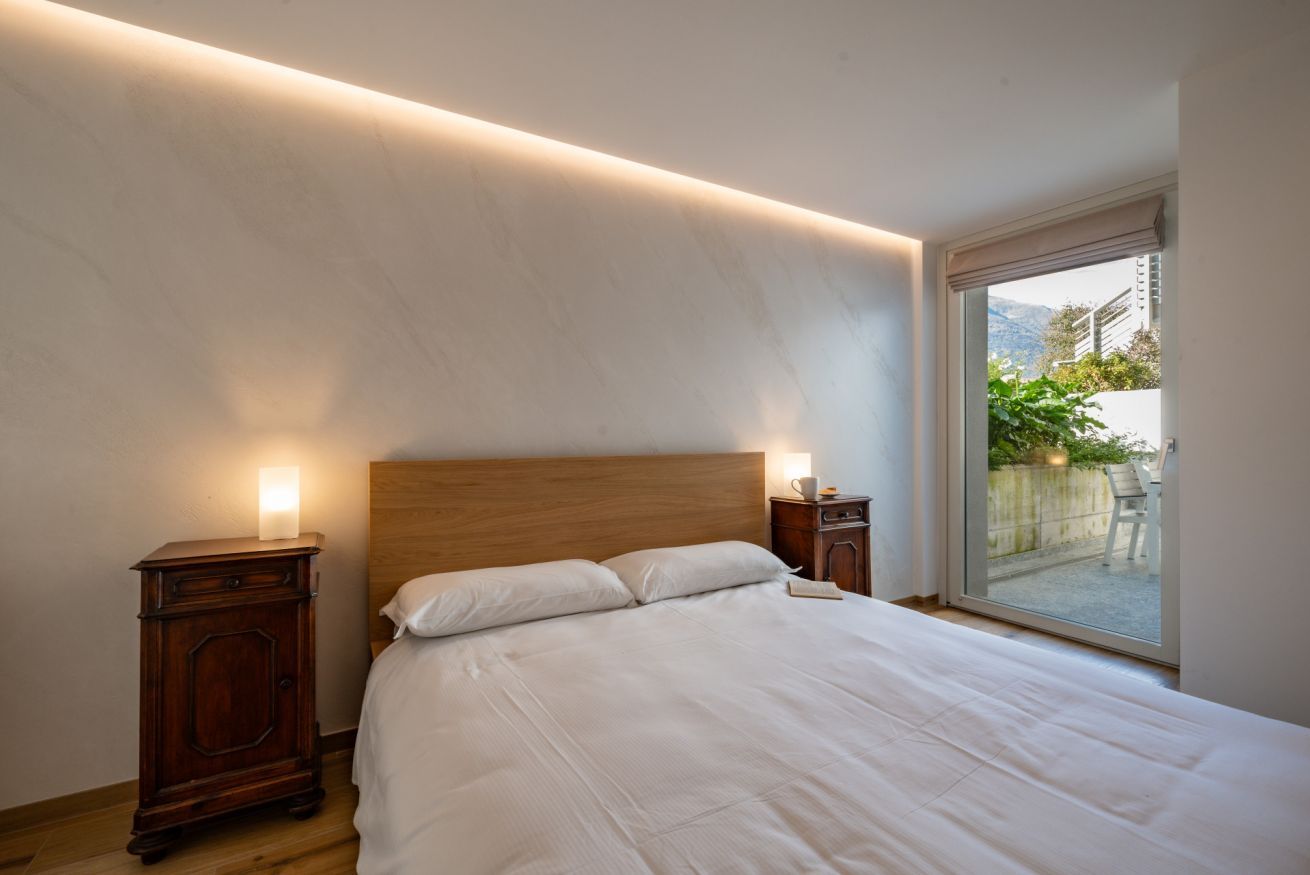 Une chambre à coucher avec une tête de lit en bois, un grand lit, des tables de chevet avec des lampes et une porte-fenêtre coulissante donnant sur un balcon.