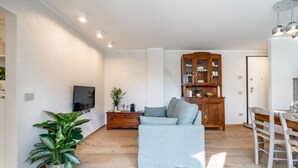 A modern living room with a sofa, a wooden cabinet, and a dining area with chairs. - Villa Sunset - with pool and large garden - few steps from the beach (Dervio)