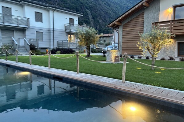 A pool area with a wooden deck, a grassy lawn, and a mountain backdrop.