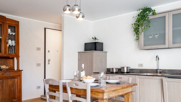 A modern kitchen with a wooden dining table, white chairs, and a built-in oven. - Villa Sunset - with pool and large garden - few steps from the beach (Dervio)