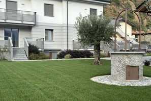 A modern two-story building with a well-maintained lawn, a stone bench, and a metal fence.