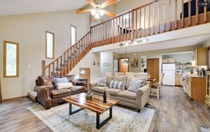 A spacious living area with a high ceiling, a wooden staircase, and a kitchen in the background. - The Hummingbirdhouse/Hottub/Kingbed/Fireplace/grill/firepit. The perfect getaway (Tobyhanna)