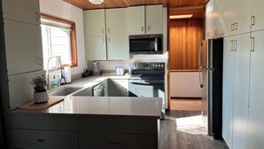 A modern kitchen with wooden ceiling, stainless steel appliances, and light-colored cabinets.